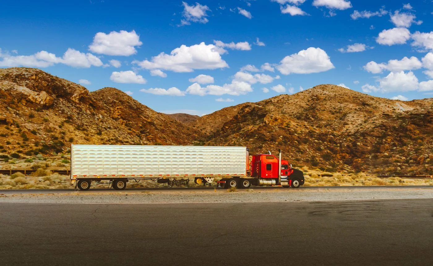 Red American semi-truck traveling on a highway through a desert landscape
